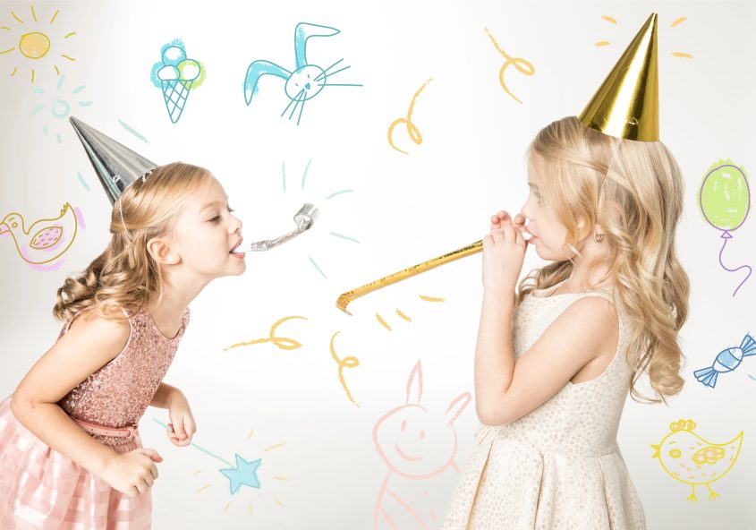 Deux petites filles en robe de fête et chapeau pointu s’amusent avec des cotillons lors d’un anniversaire, décor festif avec dessins colorés